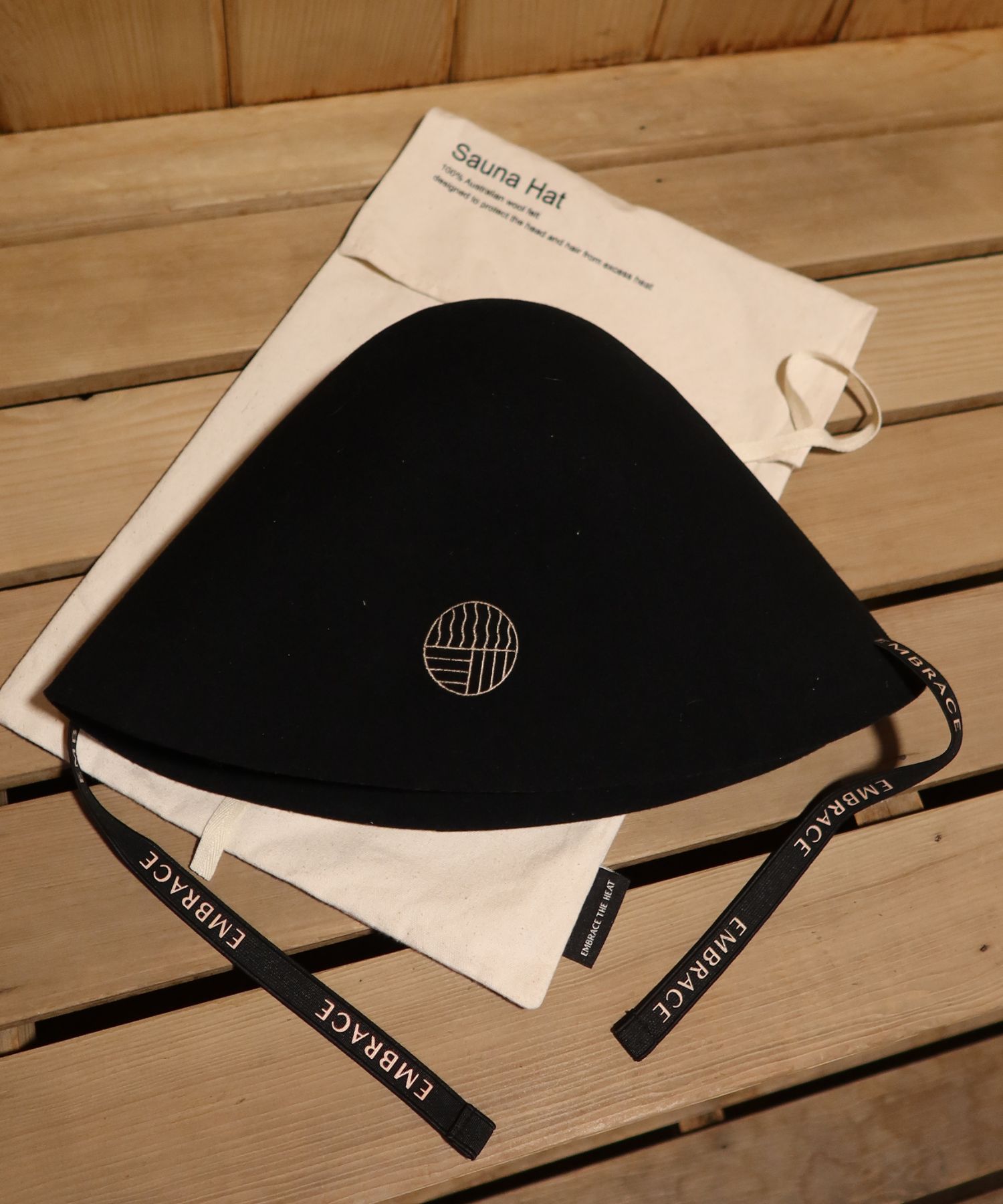 The Embrace Sauna Hat resting on its canvas pouch on a cedar sauna bench