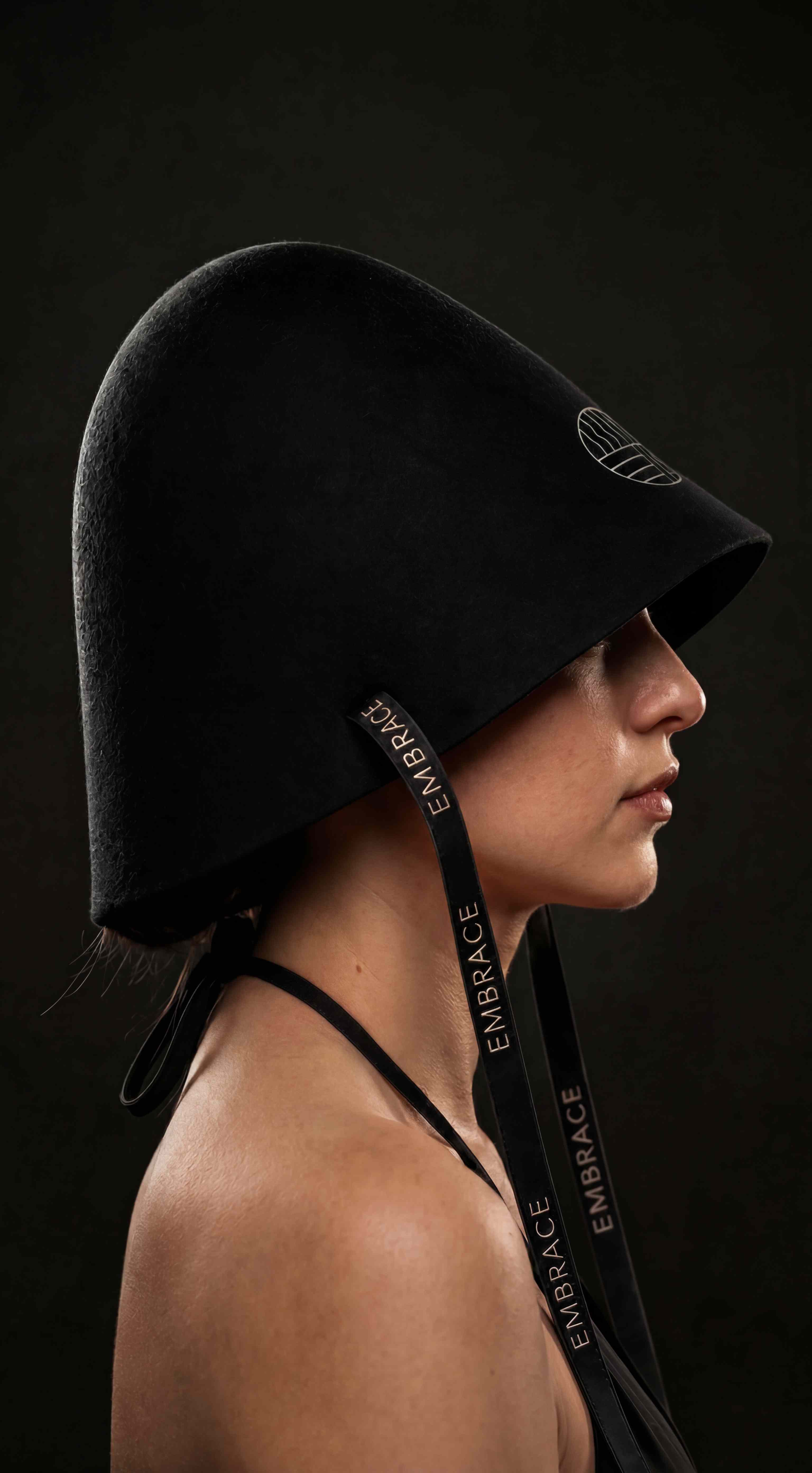 The Embrace sauna hat in neutral studio light, showing its tall felt dome, wool texture and embroidered logo