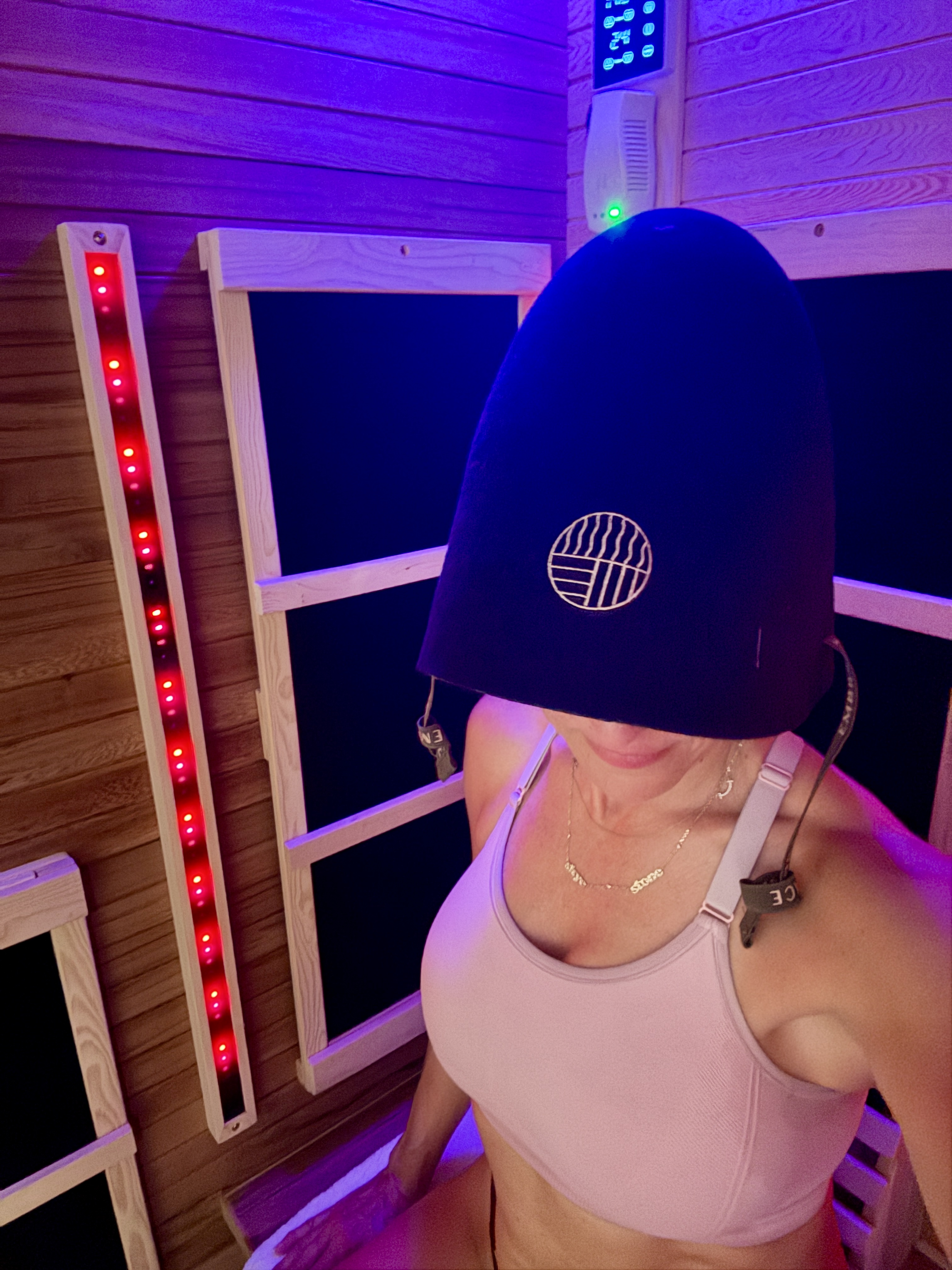 A woman in an infrared sauna with red light therapy, wearing the Embrace sauna cap